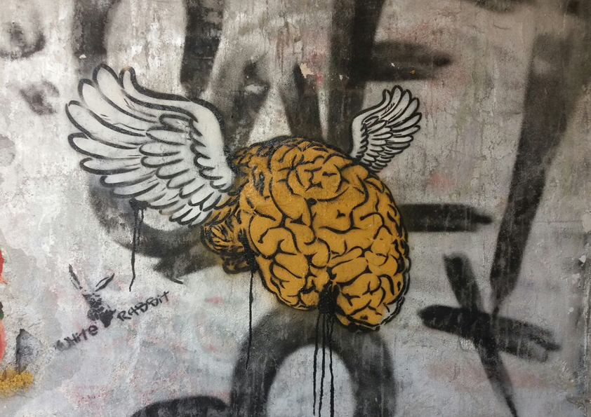 Yellow brain with white wings street art artwork by White Rabbit painted on a wall in Ibiza