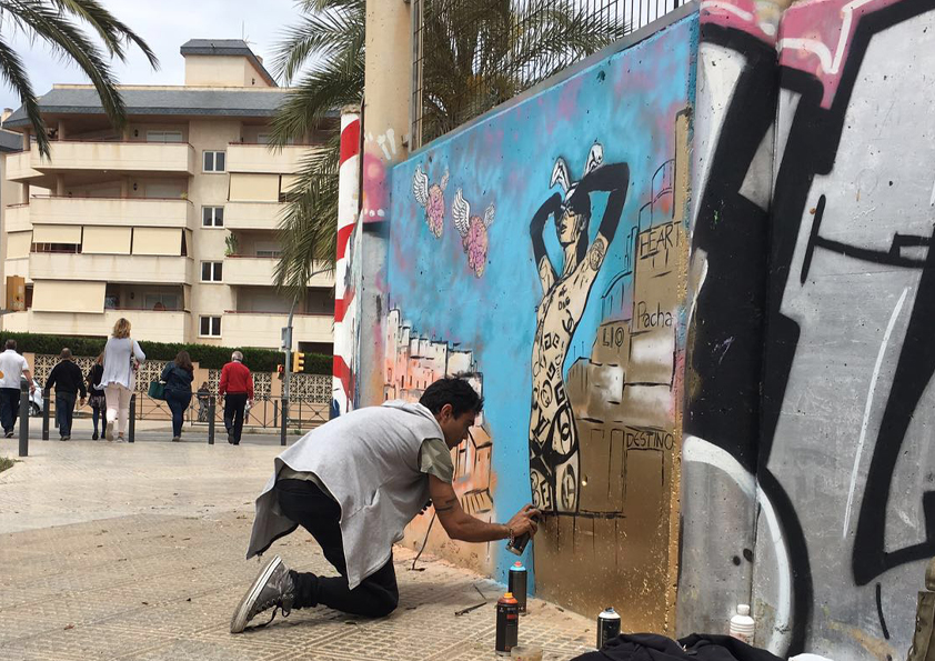 Artist White Rabbit painting a large street art mural on a wall in Ibiza